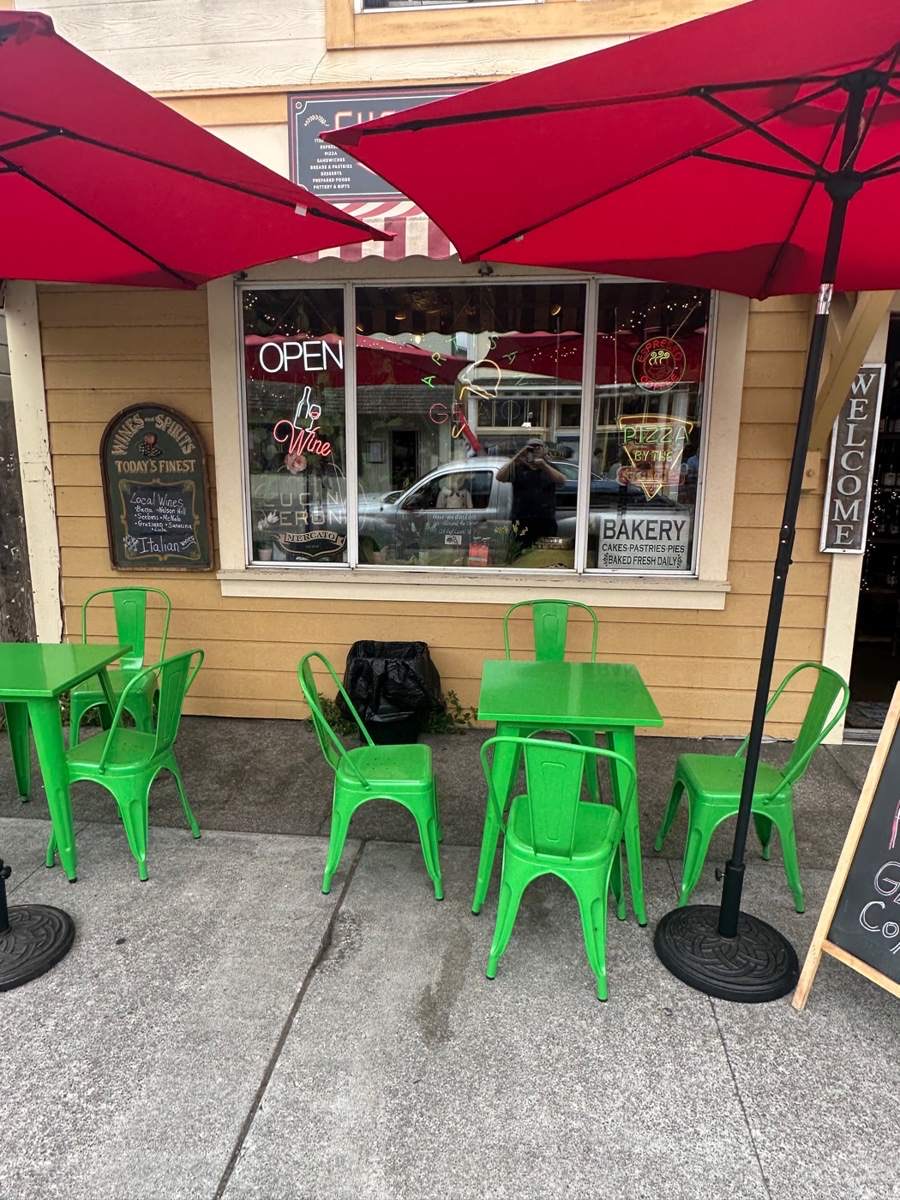 Green chairs and tables under red umbrellas in front of the Mercato