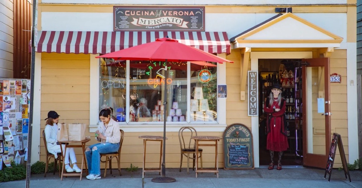 The Cucina Verona Mercato on Franklin Street: yellow storefront, striped awning, red umbrella and guests at a table out front